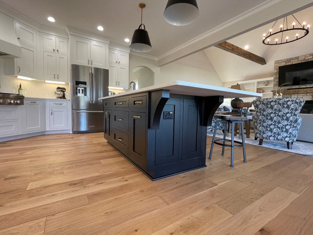 Wide-plank natural hardwood floor in an open kitchen and great room with a navy island