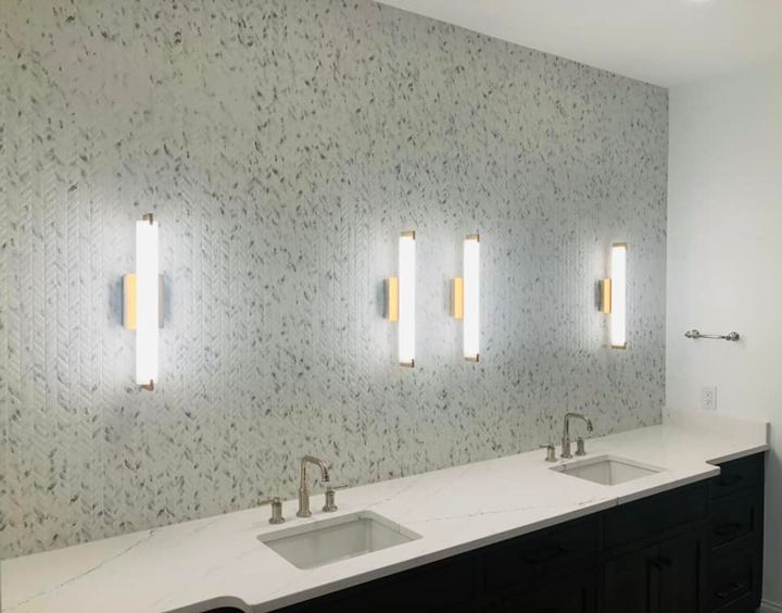 Double vanity bathroom with white chevron mosaic accent wall, quartz countertop and vertical sconce lighting