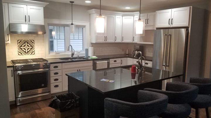 White kitchen with cream subway tile backsplash, decorative medallion inlay over the range and black granite island