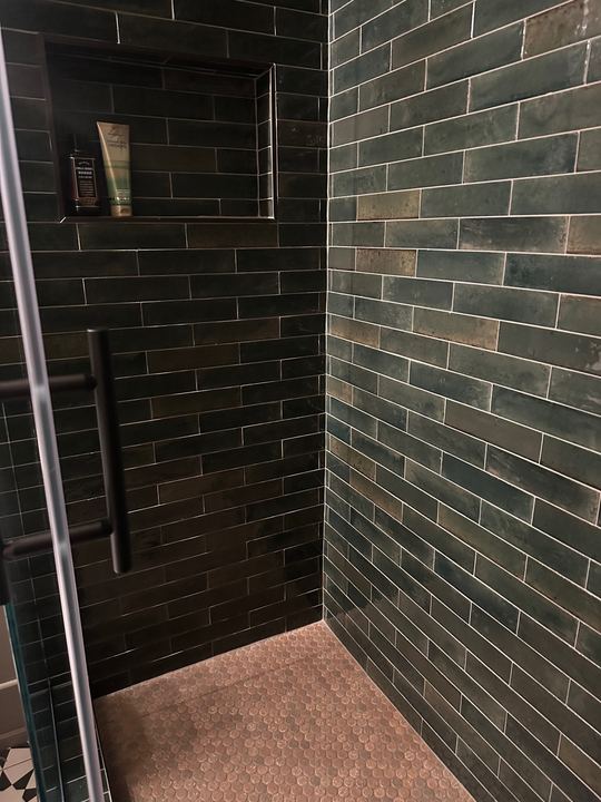 Walk-in shower with glossy dark green subway tile walls, tiled niche and copper penny round mosaic floor