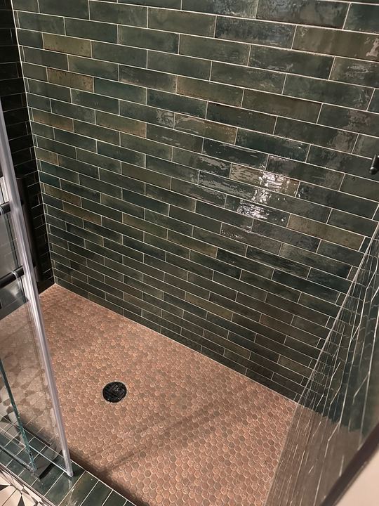 Walk-in shower with glossy green subway tile walls and tan penny-round mosaic floor