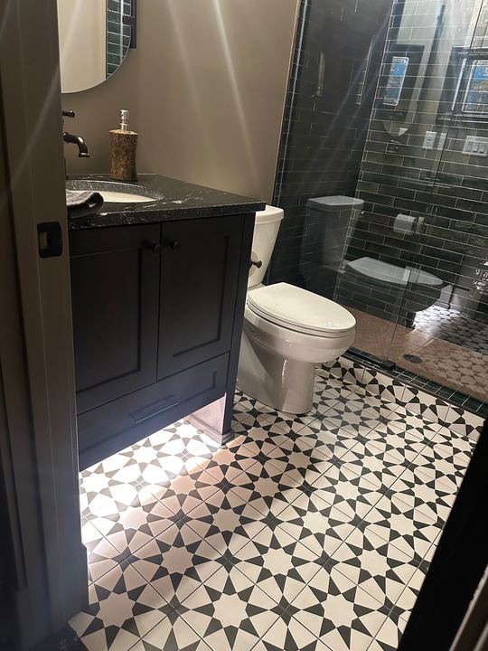 Bathroom with black and white star-pattern tile floor, dark green subway tile shower and black vanity