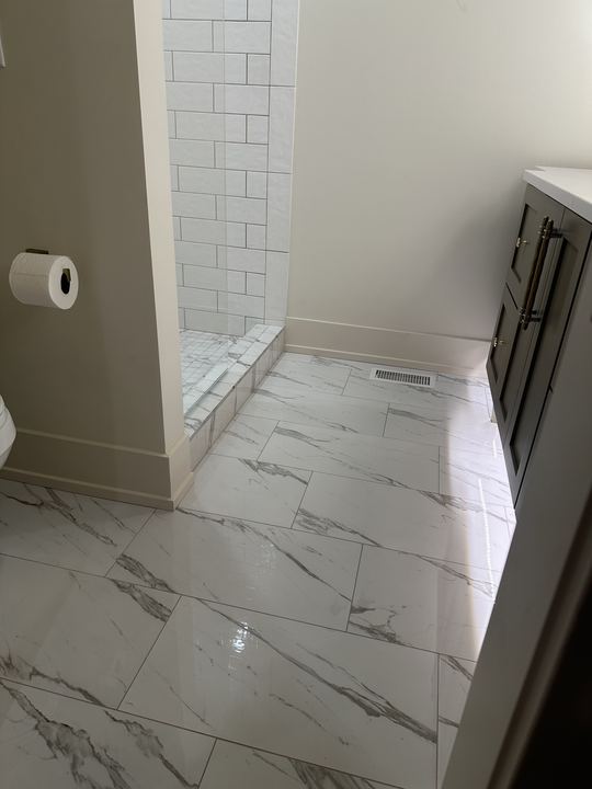 Polished marble-look porcelain tile bathroom floor with white subway shower entry and dark vanity