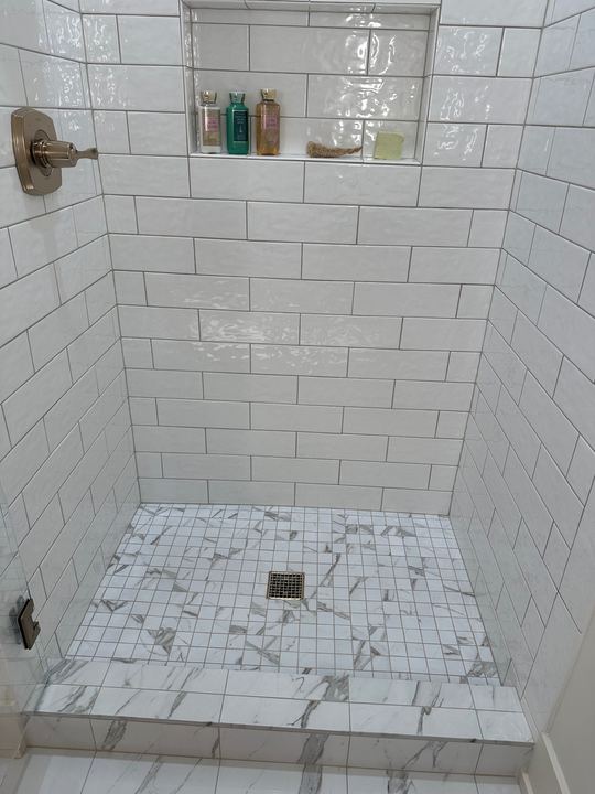 Walk-in shower with glossy white subway tile walls, marble-look mosaic floor and champagne bronze fixtures