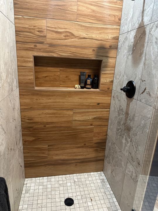 Walk-in tile shower with wood-look plank accent wall, stone-look walls, mosaic floor and black fixtures