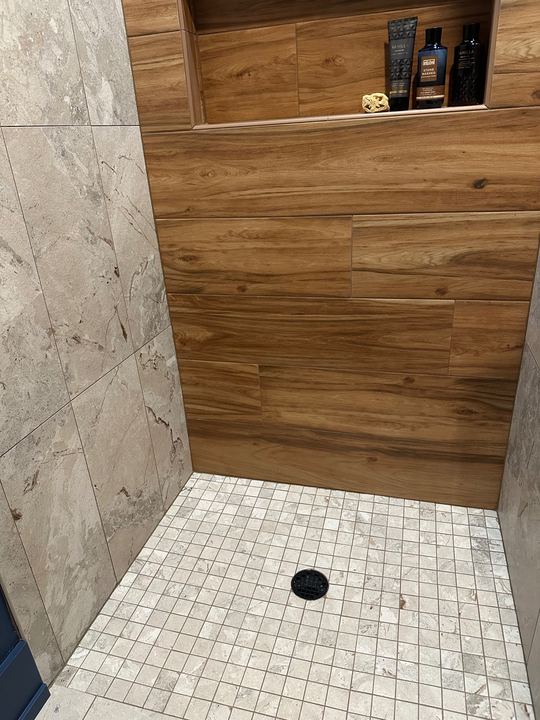 Tile shower pairing wood-look plank accent wall with marble-look walls, mosaic floor and wide shampoo niche