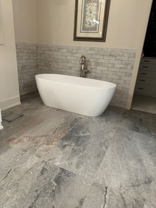 Freestanding soaker tub on gray marble-look tile floor with brick-look tile wainscot