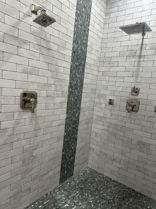Dual-head walk-in shower with white brick-look tile walls, glass mosaic waterfall accent stripe and mosaic floor