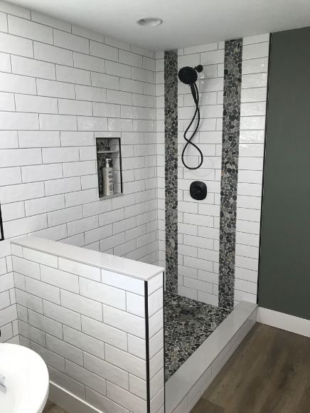 Walk-in shower with white subway tile, vertical pebble stone accent bands, matte black fixtures and tiled half wall