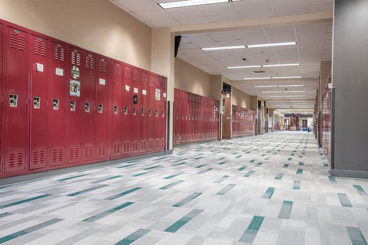 High school hallway with gray and teal plank carpet tile flooring along a wall of red lockers