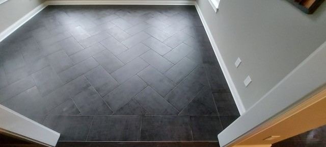 Charcoal plank tile entry floor with a herringbone center inlay bordered by straight-lay tile