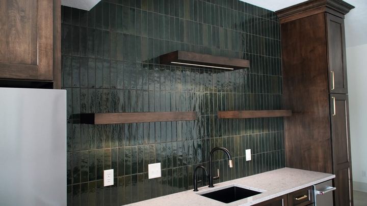 Vertically stacked glossy green tile backsplash wall with floating wood shelves and black faucet
