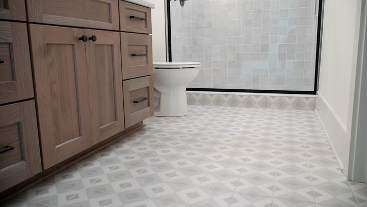 Bathroom with gray and white geometric patterned tile floor, oak vanity and square tile shower wall