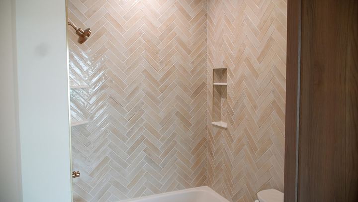 Tub surround with cream herringbone tile, recessed niche and brushed gold fixtures