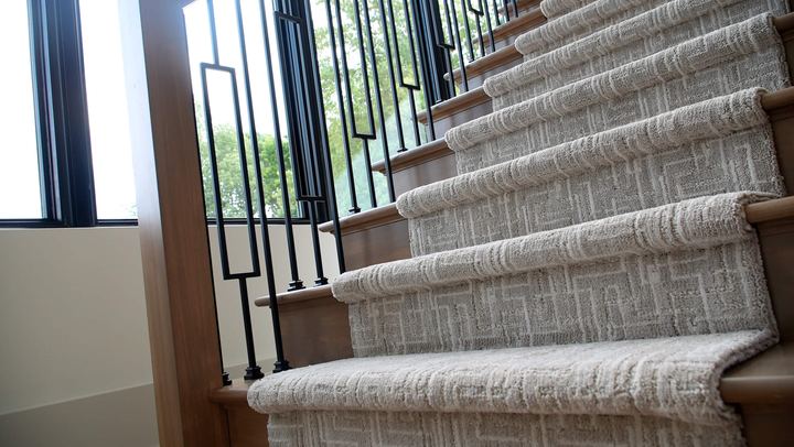 Staircase wrapped in textured gray patterned carpet with wood treads and iron balusters