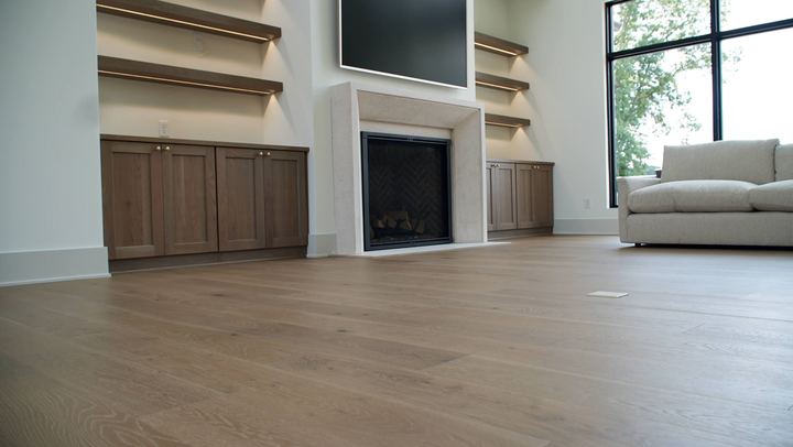 Wide-plank white oak engineered hardwood in a modern living room with stone fireplace and built-ins