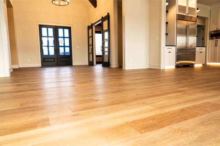 Wide-plank white oak hardwood flooring in an open great room with black French doors and vaulted ceiling