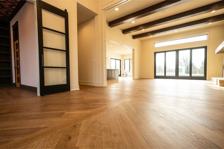 Open great room with wide plank oak hardwood flooring, dark ceiling beams and wall of windows