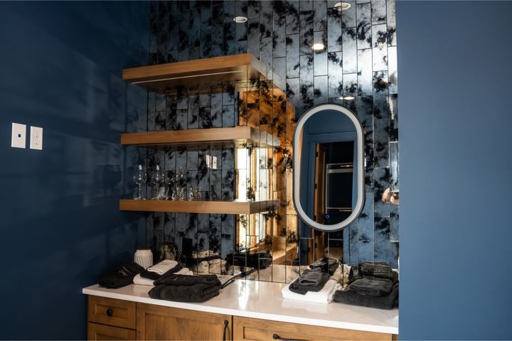 Wet bar with antiqued mirror tile backsplash, floating wood shelves, navy walls and white quartz counter
