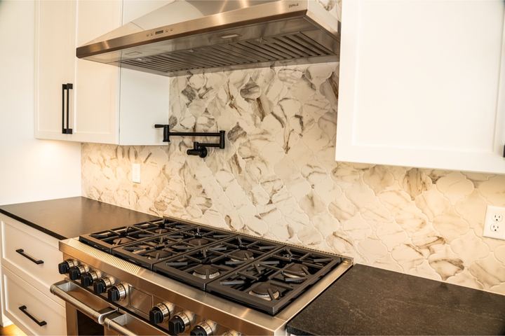 Calacatta marble arabesque mosaic backsplash behind a pro-style range with black countertops and pot filler