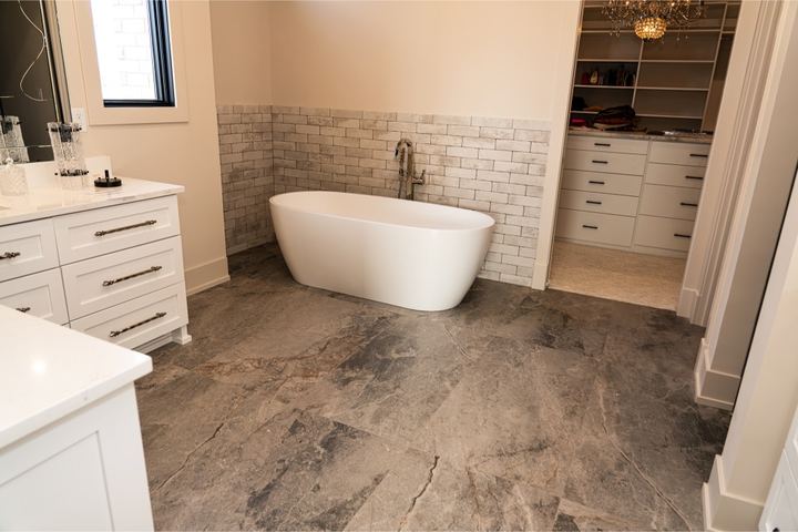 Master bathroom with gray stone-look tile floor, brick-pattern tile wainscot and freestanding soaker tub