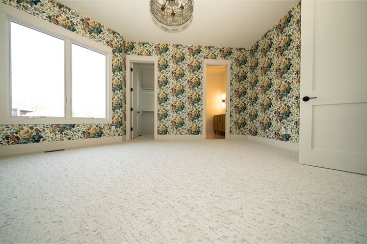 Cream patterned carpet in a bedroom with bold floral wallpaper and brass light fixture