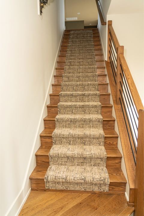 Textured patterned carpet runner on oak hardwood stairs with wood and iron railing