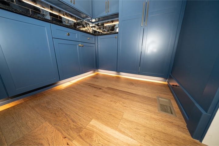 Light hickory hardwood flooring in a blue butler's pantry with under-cabinet lighting