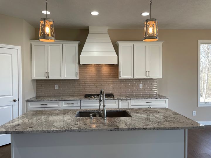 Taupe beveled subway tile backsplash in a white kitchen with granite counters and shiplap range hood