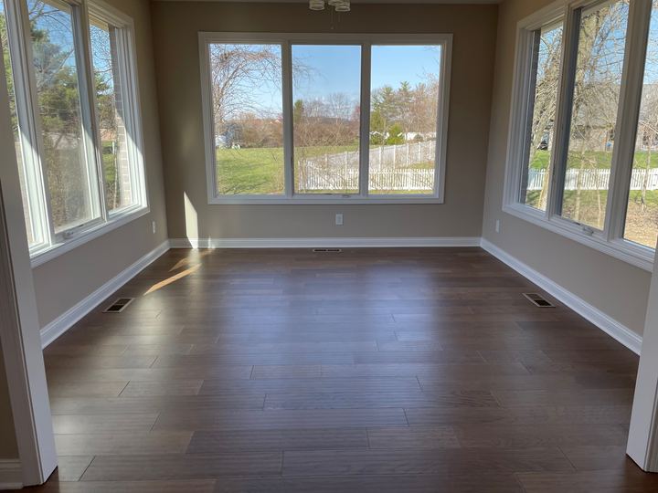 Sunlit sunroom with gray-brown wood-look plank flooring surrounded by picture windows