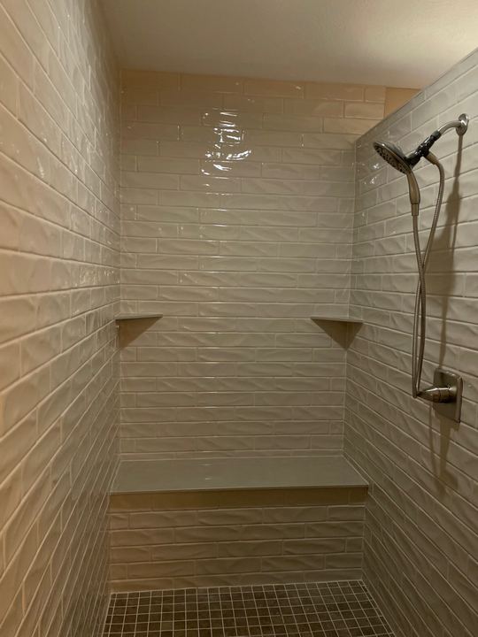 Walk-in shower with white wavy subway tile, built-in bench, corner shelves and mosaic floor