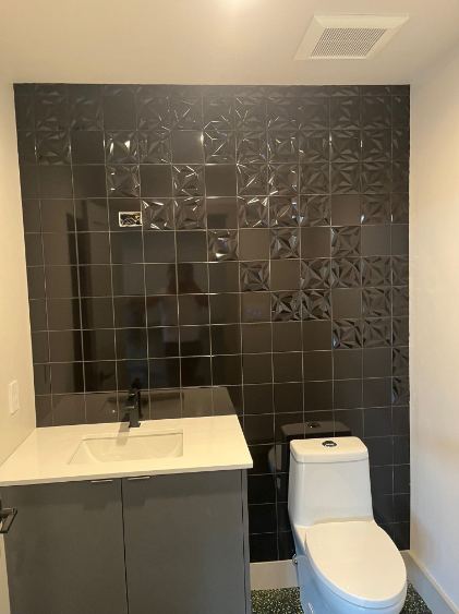 Powder room with glossy dimensional black tile accent wall, gray vanity and white countertop
