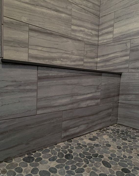 Shower with gray vein-cut stone-look tile walls, long niche and river pebble mosaic floor