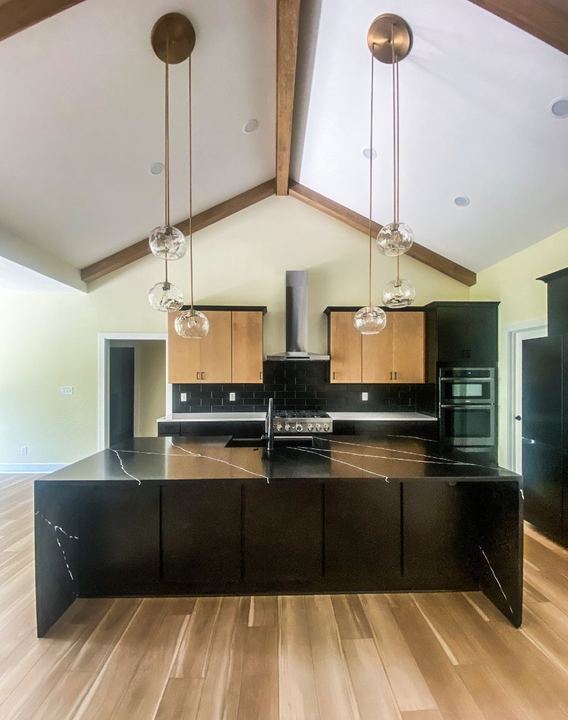 Vaulted kitchen with black subway tile backsplash, black quartz island and wood-look plank flooring