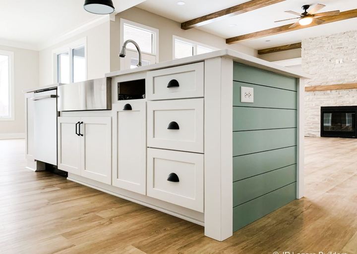 Kitchen island with farmhouse sink and shiplap end panel over warm-toned luxury vinyl plank flooring