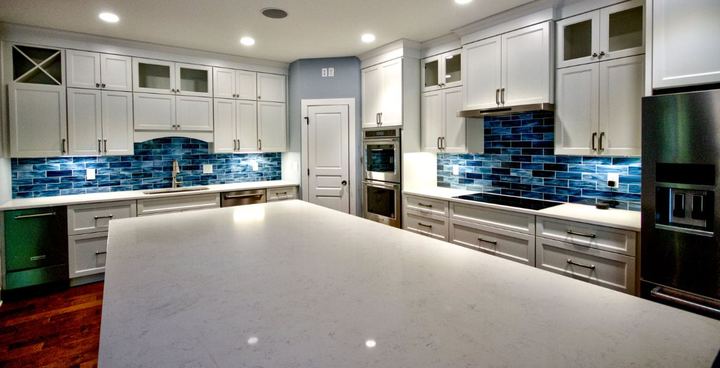 White kitchen with iridescent blue glass subway tile backsplash, quartz island and dark hardwood floor