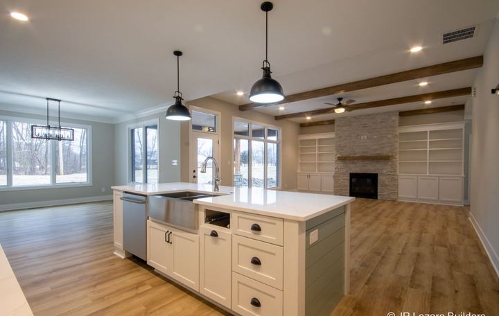 Open kitchen and living area with wood-look plank flooring, white island and stacked stone fireplace