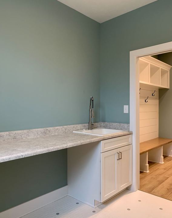 Laundry room with white hex tile floor opening to a mudroom bench with plank flooring