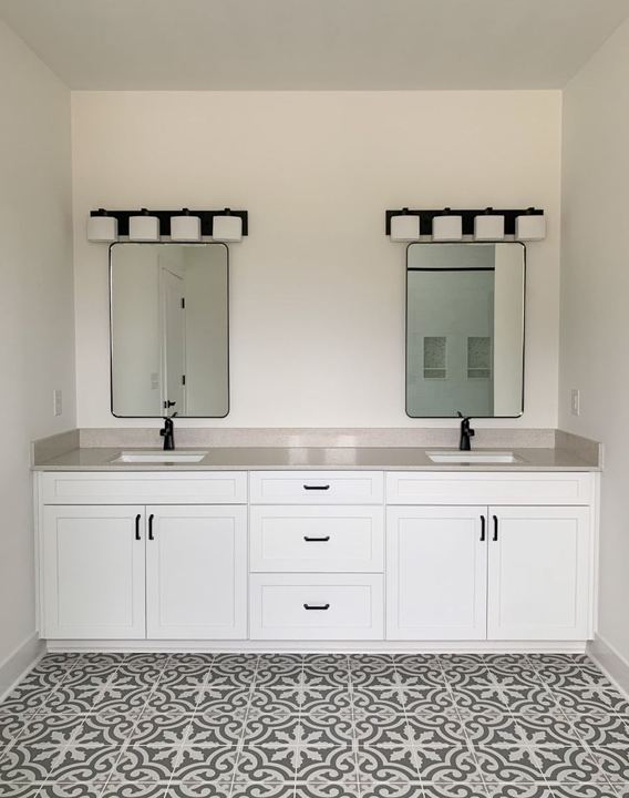 Master bathroom with gray and white encaustic patterned tile floor and white double vanity with black fixtures