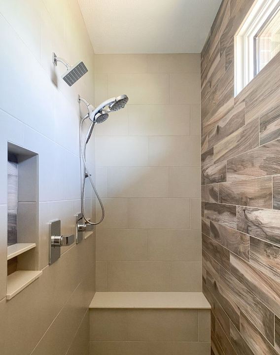 Master shower with beige large-format tile, wood-look accent wall, bench seat and double niche