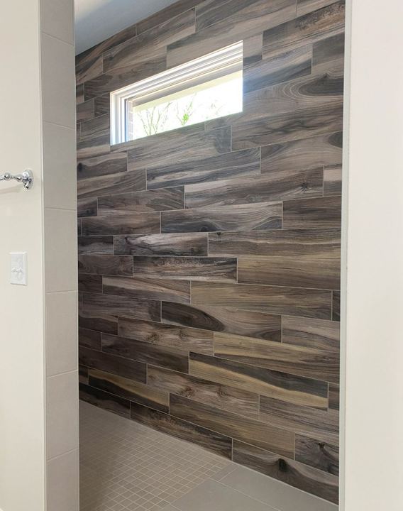 Walk-in shower with dramatic wood-look plank tile accent wall, transom window and gray mosaic floor
