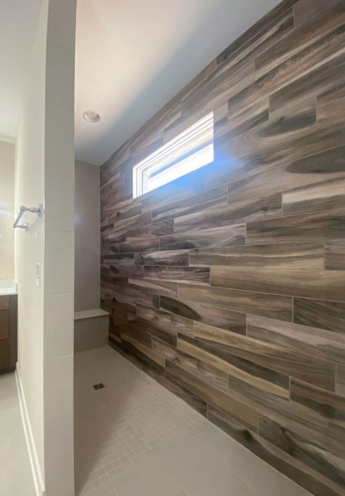 Walk-in master shower with wood-look plank tile accent wall, white mosaic floor and tiled bench