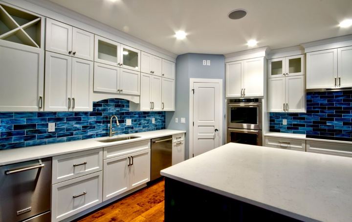 Kitchen wall run with vivid blue glass subway tile backsplash, white cabinets and hardwood floor