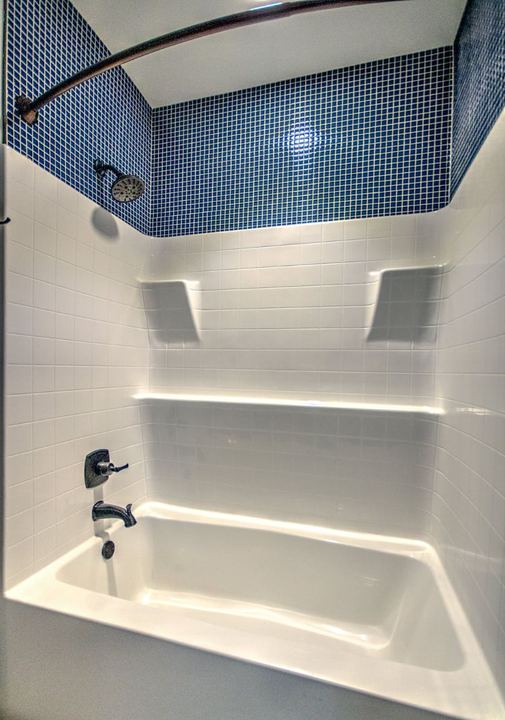 Tub and shower surround finished with navy blue square mosaic tile above and bronze fixtures