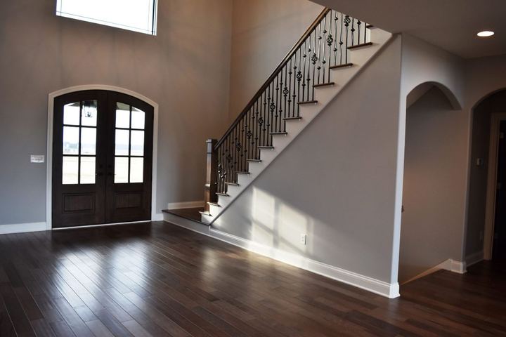 Two-story foyer with dark hardwood flooring, arched double front doors and iron-spindle staircase