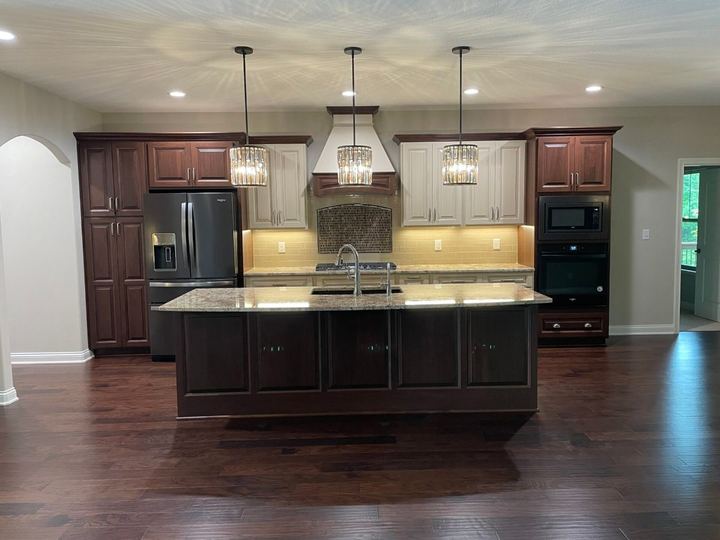 Two-tone kitchen with mosaic tile backsplash arch over the range, granite island and dark hardwood floor