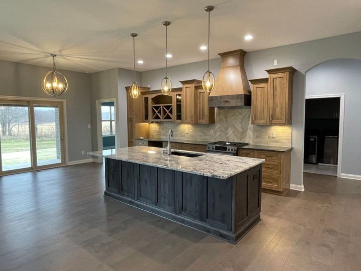 Kitchen with cream tile backsplash, herringbone accent above the range, granite-top island and hardwood floors