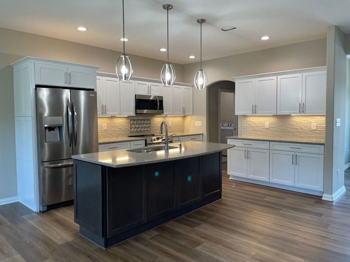 Kitchen with cream textured subway backsplash and accent insert, dark island and wood-look LVP flooring
