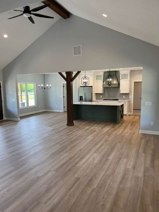 Light oak-look luxury vinyl plank across a vaulted open-concept great room and kitchen with green shiplap island