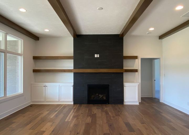 Floor-to-ceiling black tile fireplace wall with floating wood shelves and walnut hardwood floors